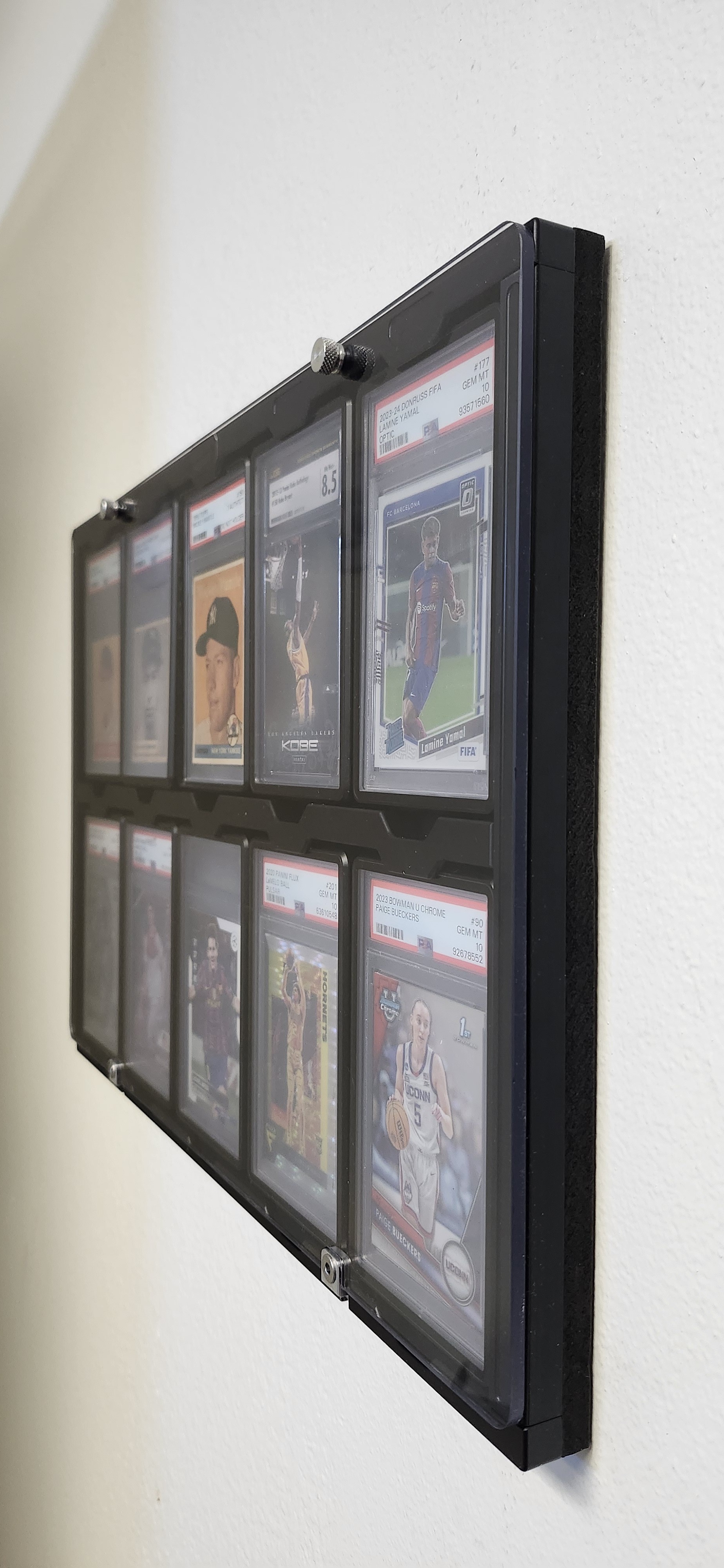 Black anodized Protected Display side angle view showing UV polycarbonate window and graded cards including Yamal and Bueckers